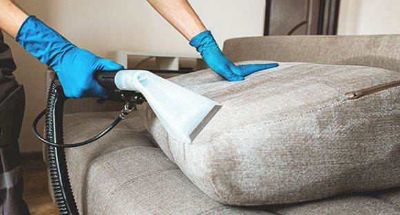 a person using an upholstery cleaning equipment to remove stains from a sofa cushion