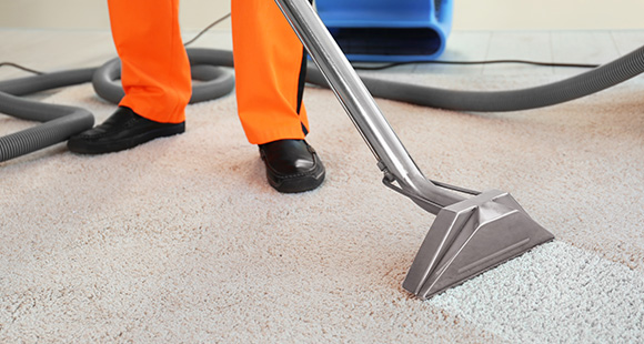 a person with orange trousers and black shoes cleaning a dirty carpet with a carpet steam cleaner