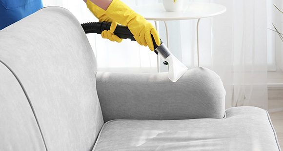 a person with yellow gloves cleaning a sofa with a vacuum cleaner